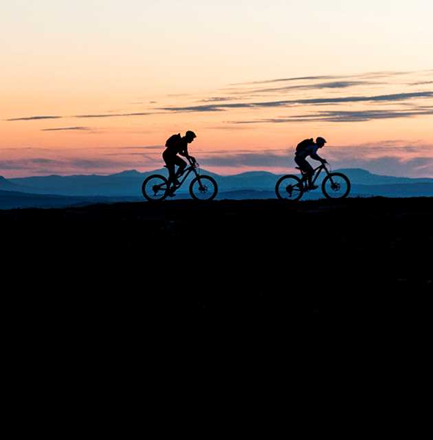 Two mountain bikers in silhouette in front of an evening sky
